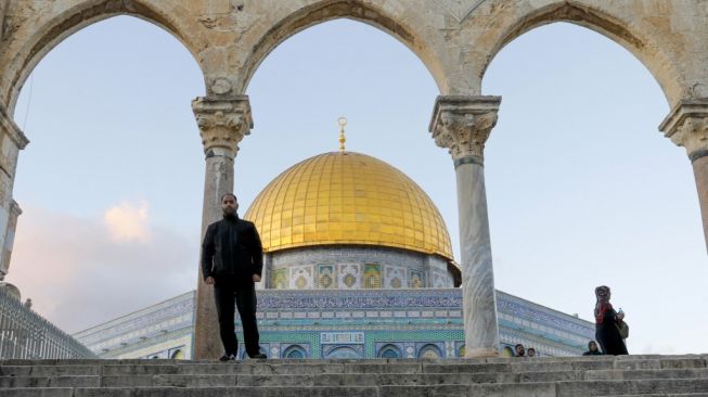 Muazin Firas Al-Qazzaz, berfoto dengan latar belakang Masjid Kubah Emas (Dome of the Rock) yang berada di Komplek Masjid Al-Aqsa, Yerusalem, Palestina. [AFP/Ahmad Gharabli]