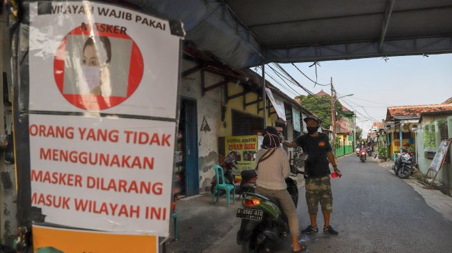 Warga Gang Kramat memeriksa pendatang didepan pintu masuk di Jalan Monumen Pancasila Sakti, Lubang Buaya, Jakarta Timur (22/4). [Suara.com/Alfian Winanto]