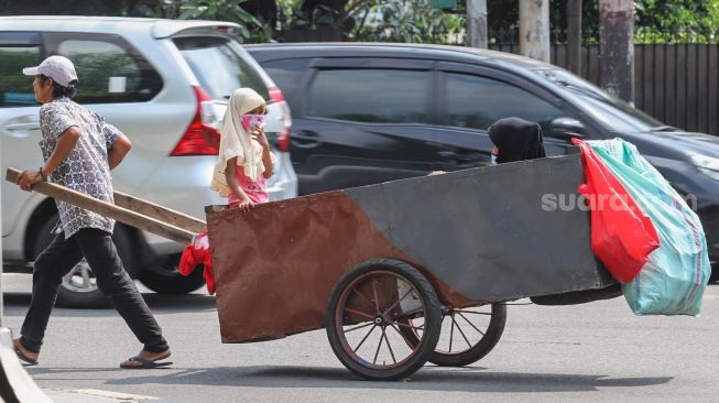 Manusia gerobak menarik gerobak yang berisi anak dan istrinya di kawasan Menteng Jakarta Pusat, Kamis (23/4). [Suara.com/Alfian Winanto]