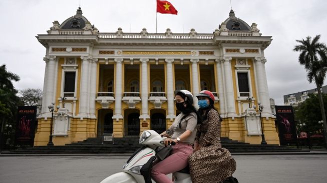 Pengendara motor mengenakan masker saat berkendara melewati Opera House di Hanoi, Vietnam, Kamis (23/4/2020). [AFP/Manan Vatsyayana]