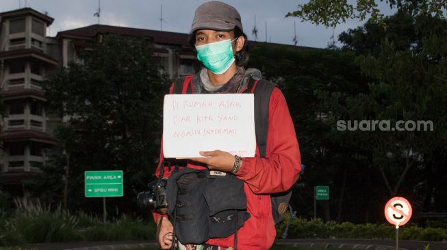 Seorang Pewarta Foto berpose sambil memperlihatkan pesannya saat difoto di Taman Lalu Lintas, Kebon Pala, Jakarta Timur, Kamis (26/3). [Suara.com/Alfian Winanto