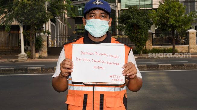 Seorang Petugas PPSU berpose sambil memperlihatkan pesannya saat difoto di daerah Cawang, Jakarta Timur, Minggu (19/4). [Suara.com/Alfian Winanto]