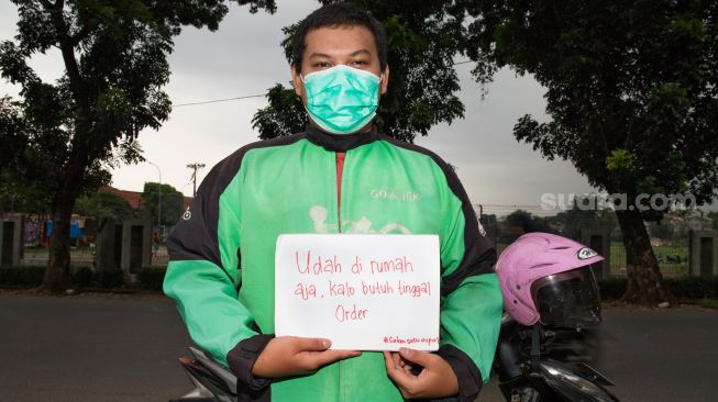 Seorang pengemudi Ojek Daring berpose sambil memperlihatkan pesannya saat difoto di daerah Taman Mini, Jakarta Timur, Sabtu (4/4) . [Suara.com/Alfian Winanto]