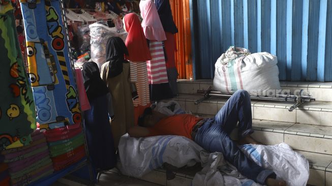 Pedagang tertidur di lapaknya di pasar Tanah Abang yang sepi pengunjung pada hari kedua di bulan suci Ramadhan akibat pandemi virus Corona (COVID-19) di Jakarta, Minggu (26/4). [Suara.com/Angga Budhiyanto]