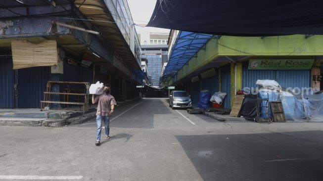 Pedagang melintas di pasar Tanah Abang yang sepi pengunjung pada hari kedua di bulan suci Ramadhan akibat pandemi virus Corona (COVID-19) di Jakarta, Minggu (26/4). [Suara.com/Angga Budhiyanto]