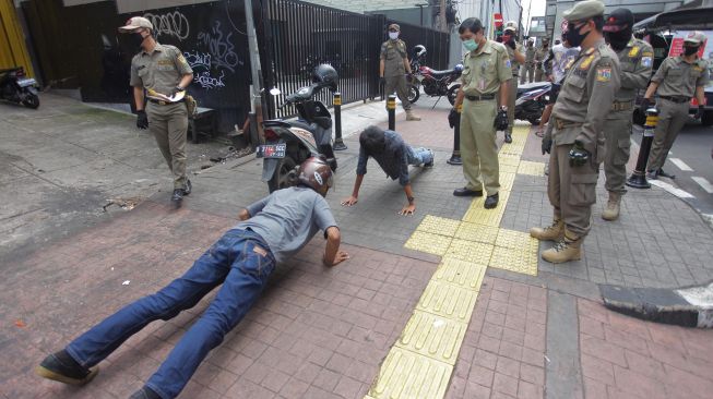 Petugas gabungan memberikan hukuman push up kepada pengendara motor yang tidak memakai masker saat razia Pembatasan Sosial Berskala Besar(PSBB) di Kawasan Jalan Fatmawati, Jakarta, Selasa (28/4).  [ANTARA FOTO/Reno Esnir]