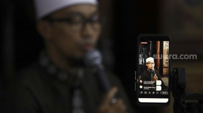 Seorang ustaz tadarus Al-Quran secara online di Masjid Agung Sunda Kelapa, Jakarta, Selasa (28/4). [Suara.com/Angga Budhiyanto]
