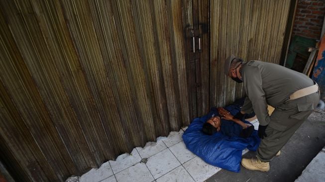 Petugas Satpol PP membangunkan seorang pengemis yang tidur di emperan toko di Jalan Dewi Sartika, Cawang, Jakarta, Rabu (29/4). [ANTARA FOTO/Aditya Pradana Putra]