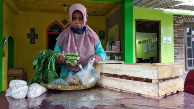 Ardiati, seorang warga Sleman, tengah menggantungkan sayur mayur gratis sebagai bantuan di bulan Ramadan selama pandemi corona di halaman rumahnya di Dusun Rajek Lor, Desa Tirtoadi, Kecamatan Mlati, Rabu (29/4/2020). - (SuaraJogja.id/Muhammad Ilham Baktora)