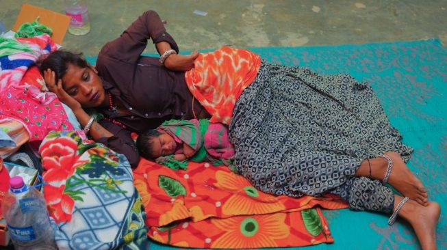 Wanita asal Negara Bagian Agartala, India, Manju Bauri, berbaring di samping bayi laki-lakinya yang lahir pada 13 April 2020 dan diberi nama Lockdown. Foto ini diambil pada, Sabtu (18/4/2020). [AFP/Abhisek Saha]