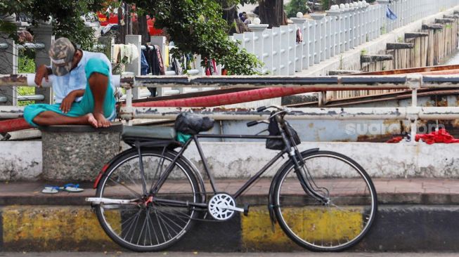 Pengojek sepeda ontel berteduh di bawah pohon menunggu penumpang di kawasan Kota Tua, Jakarta Barat, Minggu (3/5). [Suara.com/Alfian Winanto]