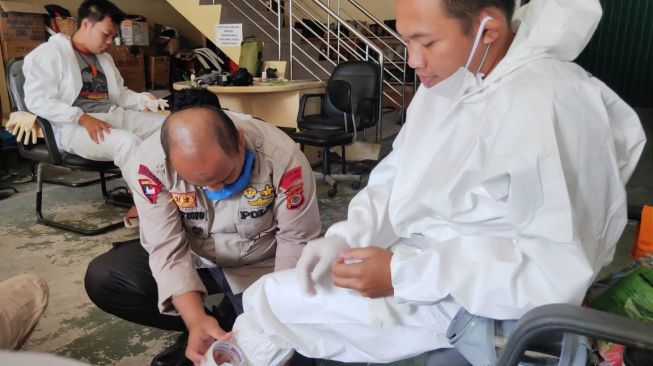 Polisi membantu petugas memasang APD berupa seragam hazmat sebelum prosesi pemakaman jenazah pasien Covid-19. - (SuaraJogja.id/HO-dok TRC BPBD DIY)