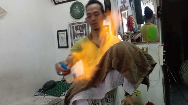 Kenyo saat melayani kustomernya di ruang pangkas. [Suara.com/Yosea Arga]