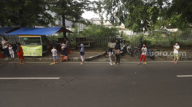 Sejumlah warga mengantre dengan menerapkan aturan jarak fisik atau 'physical distancing' untuk mendapatkan takjil gratis di Jalan Cempaka Putih Tengah, Kecamatan Cempaka Putih, Jakarta Pusat, Kamis (7/5). [Suara.com/Angga Budhiyanto]