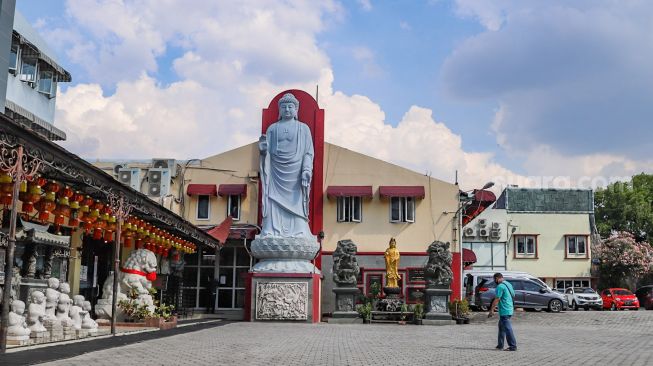 Petugas melintas didepan patung Budha di Wihara Ekayana Arama, Jakarta Barat, Kamis (7/5). [Suara.com/Alfian Winanto]