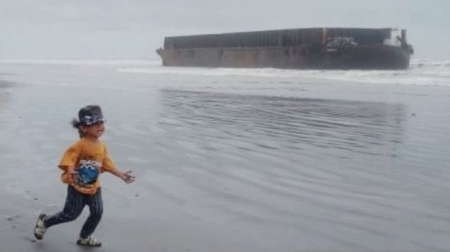 Seorang anak bermain di bibir pantai dengan latar kapal tongkang yang terdampar di kawasan Desa Peunaga Pasi, Kecamatan Meureubo, Kabupaten Aceh Barat, Jumat (8/5/2020) petang [ANTARA/Teuku Dedi Iskandar]. 