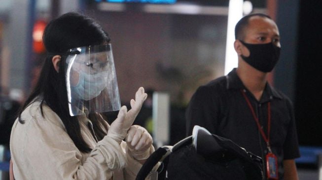 Seorang calon penumpang pesawat menggunakan pelindung wajah dan sarung tangan karet saat mengantre untuk lapor diri di Terminal 3 Bandara Soekarno Hatta, Tangerang, Banten, Minggu (10/5).  [ANTARA FOTO/Muhammad Iqbal]