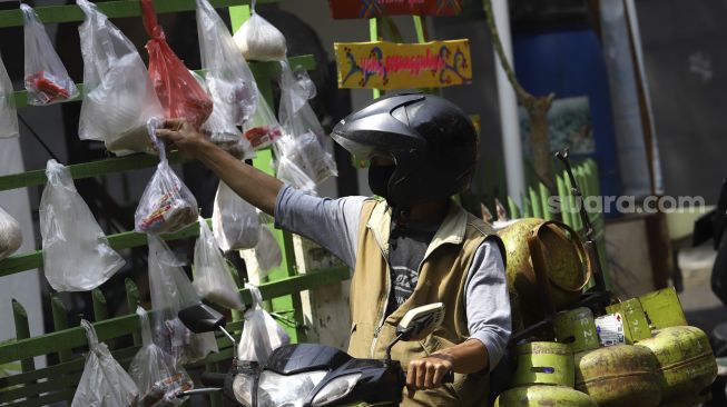 Pedagang keliling mengambil sembako yang digantung di rak kayu di kawasan Rawa Barat, Jakarta Selatan, Kamis (14/5). [Suara.com/Angga Budhiyanto]