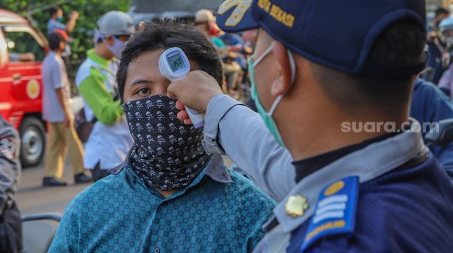 Petugas mengecek suhu tubuh pengendara sepeda motor yang akan memasuki Bekasi dengan Thermo Gun di Check Point PSBB Pondok Gede, Bekasi, Jawa Barat, Kamis (15/5). [Suara.com/Alfian Winanto]