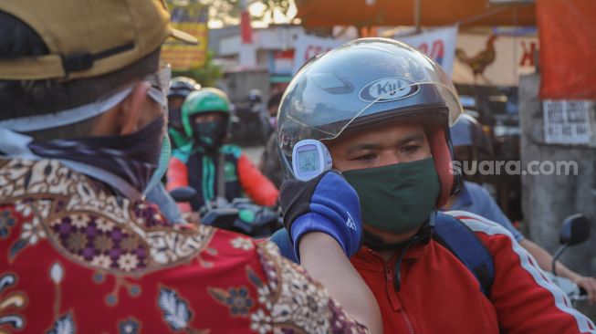 Petugas mengecek suhu tubuh pengendara sepeda motor yang akan memasuki Bekasi dengan Thermo Gun di Check Point PSBB Pondok Gede, Bekasi, Jawa Barat, Kamis (15/5). [Suara.com/Alfian Winanto]