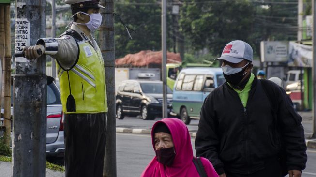 Warga melintas di samping sebuah patung polisi lalu lintas yang dipasangkan masker di Bandung, Jawa barat, Jumat (15/5/2020). [ANTARA FOTO/Novrian Arbi]