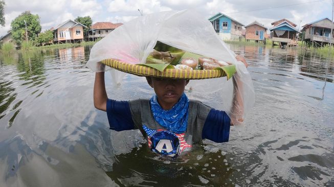 Seorang bocah menerobos banjir luapan Sungai Batanghari yang menggenangi permukiman untuk berjualan di Pelayangan, Jambi, Kamis (14/5).   [ANTARA FOTO/Wahdi Septiawan]