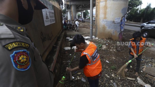 Warga yang terjaring razia penindakan pelanggaran aturan Pembatasan Sosial Berskala Besar (PSBB) oleh Tim Satgas Gugus Tugas COVID-19 menjalani hukuman dengan cara membersihkan sampah di kawasan Cilandak, Jakarta, Selasa (19/5). [Suara.com/Angga Budhiyanto]
