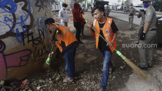 Warga terjaring razia penindakan pelanggaran aturan Pembatasan Sosial Berskala Besar (PSBB) oleh Tim Satgas Gugus Tugas COVID-19 menjalani hukuman dengan cara membersihkan sampah di kawasan Cilandak, Jakarta, Selasa (19/5). [Suara.com/Angga Budhiyanto]