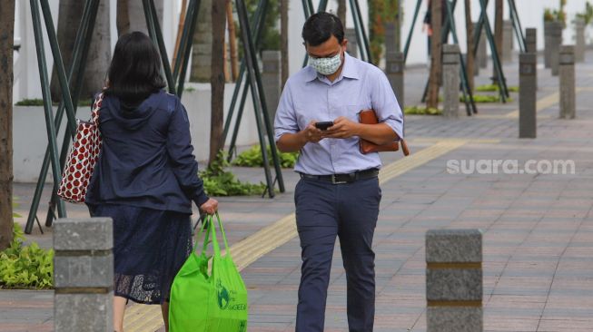 Pekerja kantoran melintas di kawasan Sudirman, Jakarta Pusat, Selasa (19/5). [Suara.com/Alfian Winanto]
