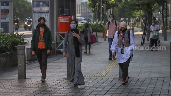 Seorang pekerja kantoran melintas di trotoar kawasan Sudirman, Jakarta Pusat, Selasa (19/5).  [Suara.com/Alfian Winanto]