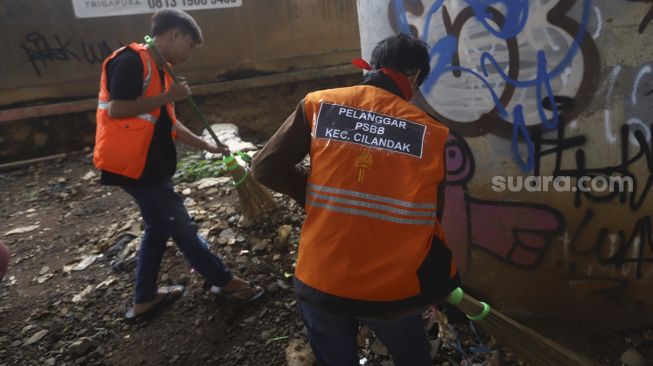 Warga yang terjaring razia penindakan pelanggaran aturan Pembatasan Sosial Berskala Besar (PSBB) oleh Tim Satgas Gugus Tugas COVID-19 menjalani hukuman dengan cara membersihkan sampah di kawasan Cilandak, Jakarta, Selasa (19/5). [Suara.com/Angga Budhiyanto]