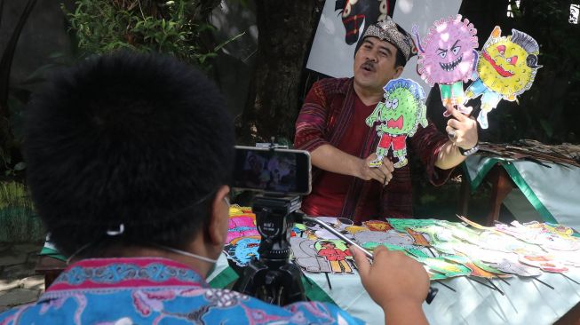 Kepala sekolah SD Katolik Frateran II Fx. Luhkita Heru Pratama memainkan wayang COVID-19 untuk disampaikan secara daring kepada murid-muridnya di Kota Kediri, Jawa Timur, Jumat (22/5).  [ANTARA FOTO/Prasetia Fauzani]
