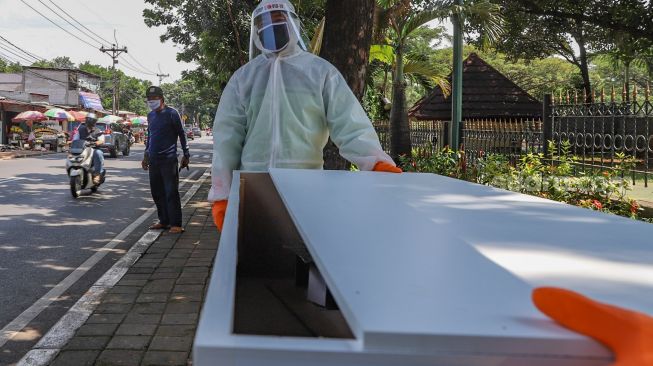 Petugas tempat pemakaman umum (TPU) membawa peti mati  di TPU Tanah Kusir, Jakarta Selatan, Sabtu (23/5). [Suara.com/Alfian Winanto]
