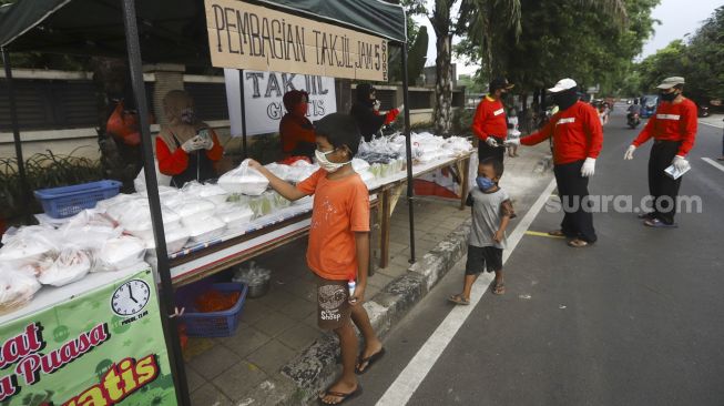 Sejumlah warga mengantre dengan menerapkan aturan jarak fisik atau 'physical distancing' untuk mendapatkan takjil gratis di Jalan Cempaka Putih Tengah, Kecamatan Cempaka Putih, Jakarta Pusat, Rabu (6/5). [Suara.com/Angga Budhiyanto]