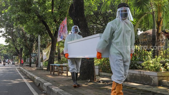 Petugas tempat pemakaman umum (TPU) membawa peti mati  di TPU Tanah Kusir, Jakarta Selatan, Sabtu (23/5). [Suara.com/Alfian Winanto]
