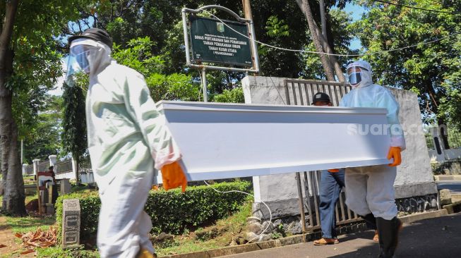 Petugas tempat pemakaman umum (TPU) membawa peti mati  di TPU Tanah Kusir, Jakarta Selatan, Sabtu (23/5). [Suara.com/Alfian Winanto]
