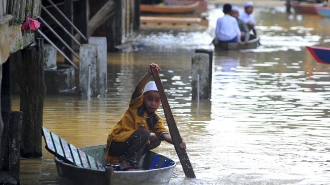 Sejumlah anak menggunakan perahu melintasi jalan permukiman yang terendam banjir luapan Sungai Batanghari saat perayaan Idul Fitri 1441 Hijriah di Tahtul Yaman, Pelayangan, Jambi, Minggu (24/5). [ANTARA FOTO/Wahdi Septiawan]