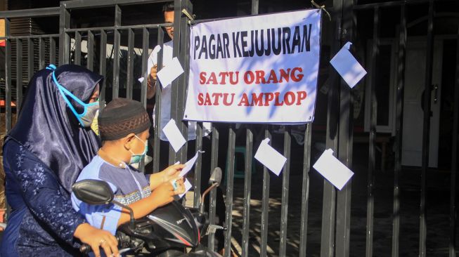 Warga mengambil amplop berisi uang yang dipasang warga di pagar depan rumah di kawasan Kureksari, Waru, Sidoarjo, Jawa Timur, Minggu (24/5).  [ANTARA FOTO/Umarul Faruq]