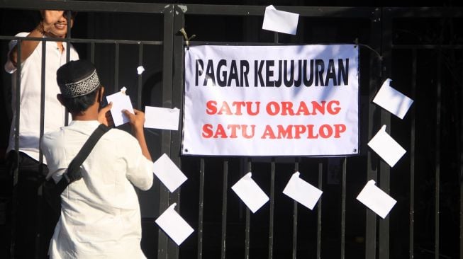 Warga mengambil amplop berisi uang yang dipasang warga di pagar depan rumah di kawasan Kureksari, Waru, Sidoarjo, Jawa Timur, Minggu (24/5).  [ANTARA FOTO/Umarul Faruq]