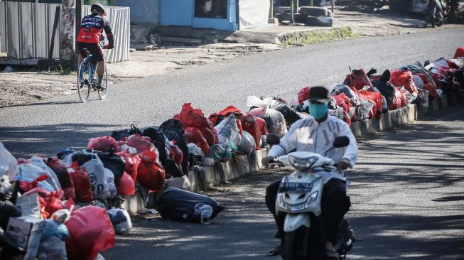 Pengendara melintas di dekat sampah yang menumpuk di pembatas jalan di Ciledug, Tangerang, Banten, Senin (25/5). [ANTARA FOTO/Rivan Awal Lingga]