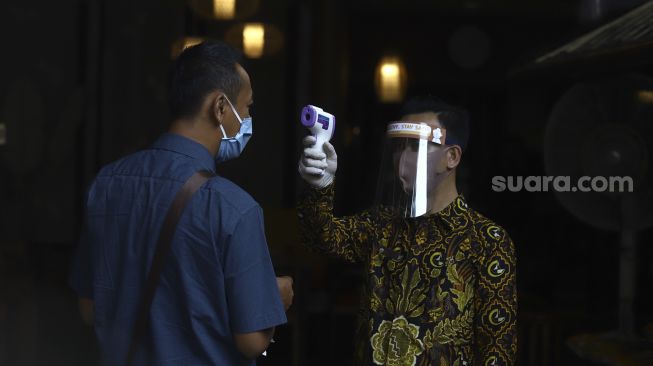 Waiters using face shields, masks and gloves check the body temperature of a prospective customer at a restaurant in the Pajajaran area, Bogor City, West Java, Friday (29/5). [Suara.com/Angga Budhiyanto]