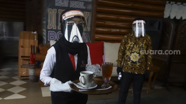 Pelayan menggunakan alat pelindung wajah, masker dan sarung tangan saat membawa pesanan pelanggan di salah satu rumah makan di kawasan Pajajaran, Kota Bogor, Jawa Barat, Jumat (29/5). [Suara.com/Angga Budhiyanto]