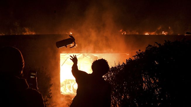 Seorang demonstran melemparkan alat pemadam kebakaran ke gedung yang terbakar saat demonstrasi di Minneapolis, Minnesota, Jumat (29/5). [Chandan Khanna/ AFP]