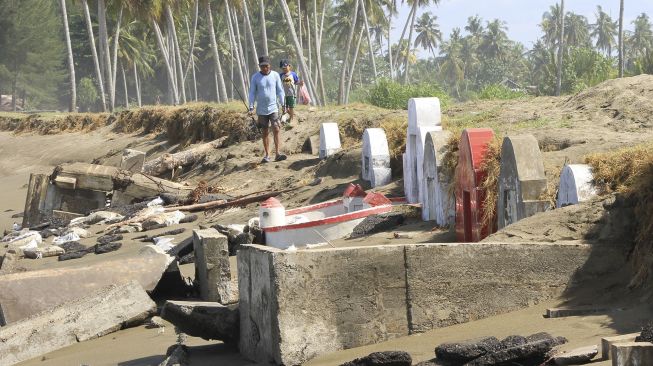 Warga melintas di samping makam etnis Tionghoa yang rusak akibat gelombang pasang di Desa Suak Ribee, Kecamatan Johan Pahlawan, Aceh Barat, Aceh, Sabtu (30/5). [ANTARA FOTO/Syifa Yulinnas]