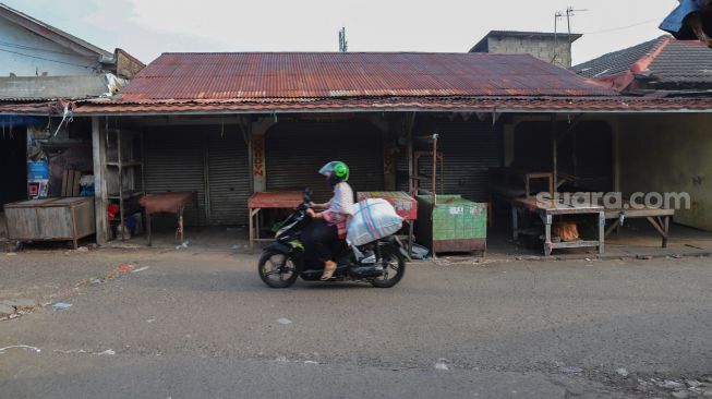 Pedagang melintas didepan  deretan warung tutup di Pasar Cisalak, Depok, Jawa Barat, Minggu (31/5). [Suara.com/Alfian Winanto]