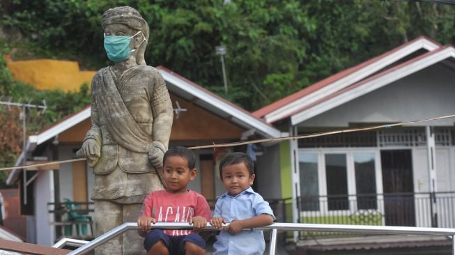 Anak-anak bermain di dekat patung Syamsul Bahri yang dipasangkan masker di Batang Arau, Padang, Sumatera Barat, Sabtu (30/5). [ANTARA FOTO/Iggoy el Fitra]