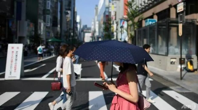 Pejalan di Jepang menatap layar ponsel sambil menyeberang. (AFP/CHARLY TRIBALLEAU)