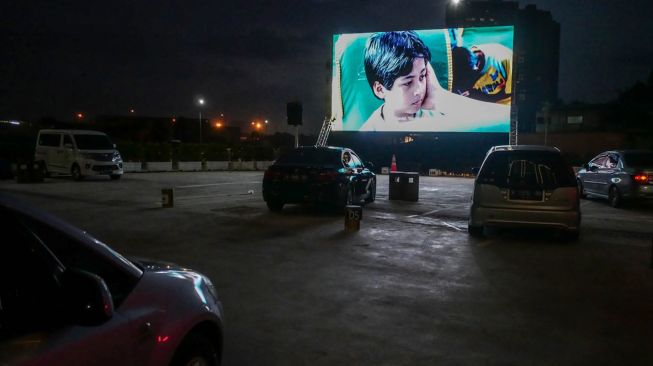 Warga menonton film yang ditampilkan di layar drive-in cinema di area parkir Meikarta Cikarang, Jawa Barat, Selasa (2/6). [Anadolu/ Anton Raharjo] 