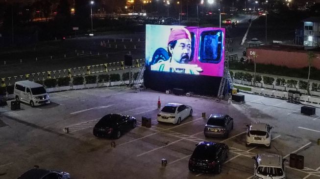 Warga menonton film yang ditampilkan di layar drive-in cinema di area parkir Meikarta Cikarang, Jawa Barat, Selasa (2/6). [Anadolu/ Anton Raharjo] 