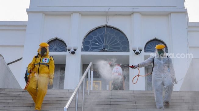 Petugas menyemprotkan cairan disinfektan area luar  Masjid Agung Al-Azhar, Jakarta Selatan, Rabu (3/6). [Suara.com/Alfian Winanto]